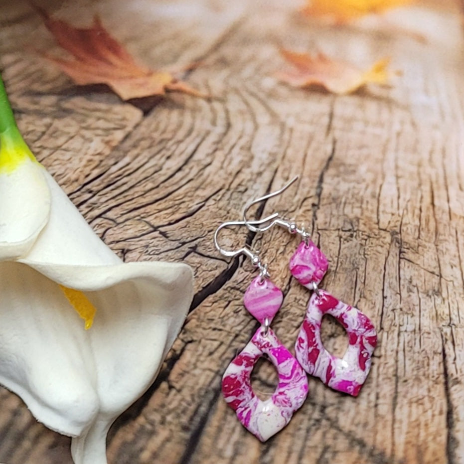 Boucles d’oreilles Rétro-chic à pendentifs ajourés aux contours ondulés, présentées près d’un arum blanc sur un décor boisé.