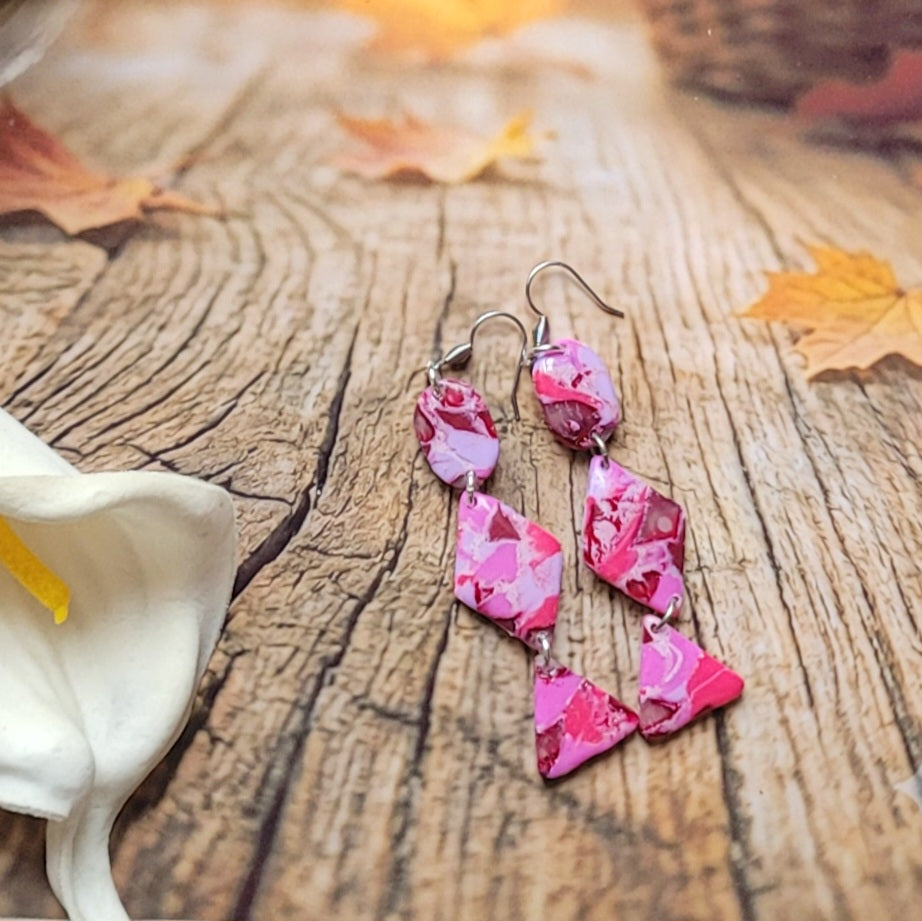 Vue d’ensemble des boucles d’oreilles Rétro-chic à trois formes articulées, disposées sur un décor boisé à côté d’un arum blanc.