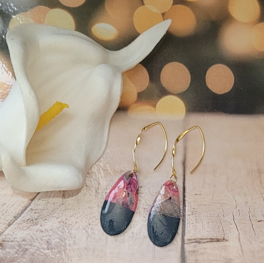  Paire de boucles Éclipse près d’un arum blanc, sur un décor de bois clair avec des lumières dorées floues en arrière-plan.