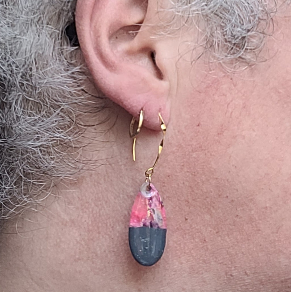  Boucle d’oreille Éclipse portée, montrant sa longue attache dorée et son pendentif en goutte rose et gris foncé