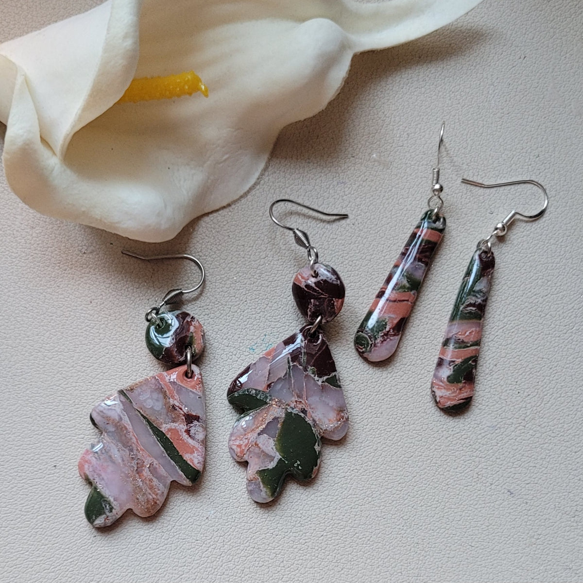  Les deux modèles de boucles d’oreilles Flora, Feuille et Longues, présentés ensemble sur fond clair près d’un arum blanc
