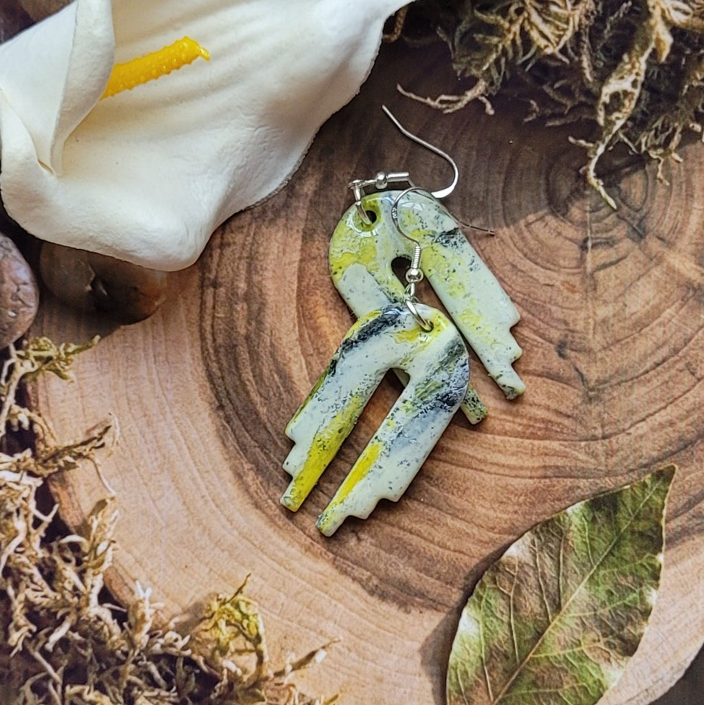 Boucles d’oreilles Empire légèrement superposées sur une tranche de bois, montrant les variations des marbrures et la forme découpée des pendentifs.