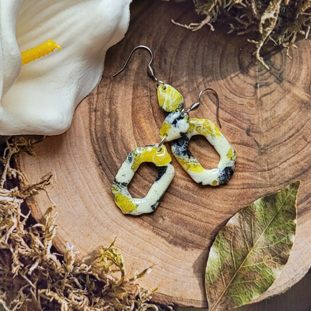 Boucles Aquarelle vanillée disposées en biais sur une tranche de bois, montrant les anneaux reliant les petits éléments aux pendentifs ajourés.