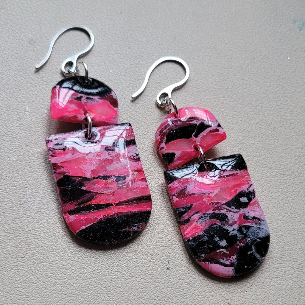  Boucles d’oreilles pendantes Nyméria en pâte polymère et résine, marbrées rose et noir, photographiées à plat.