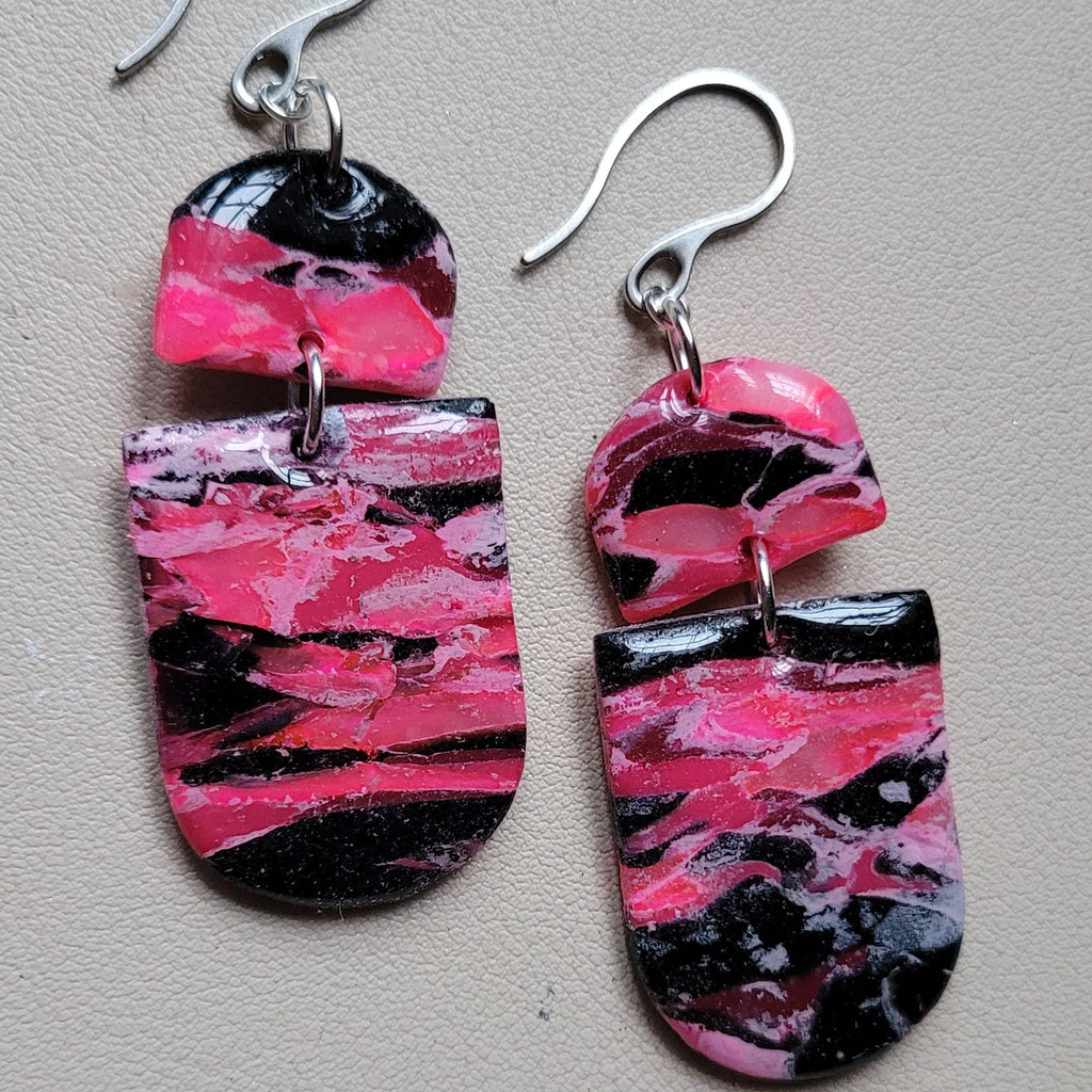  Boucles d’oreilles pendantes Nyméria en pâte polymère et résine, marbrées rose et noir, photographiées à plat.