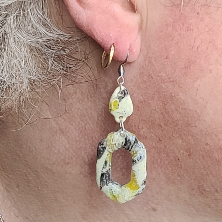 Boucle d’oreille Aquarelle vanillée portée, montrant ses deux éléments articulés, son pendentif géométrique ajouré et son crochet argenté.