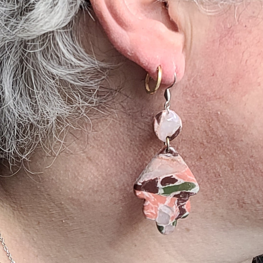  Boucle d’oreille Flora Feuille portée, montrant le petit élément rond et le pendentif en feuille stylisée aux marbrures roses, mauves et vertes.