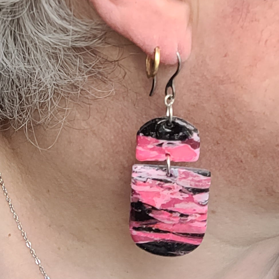  Boucles d’oreilles pendantes Nyméria en pâte polymère et résine, marbrées rose et noir, photographiées portées.