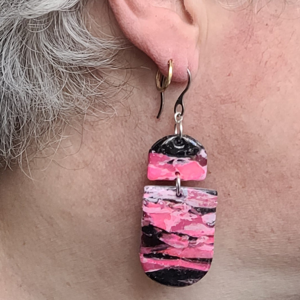  Boucles d’oreilles pendantes Nyméria en pâte polymère et résine, marbrées rose et noir, photographiées portées.