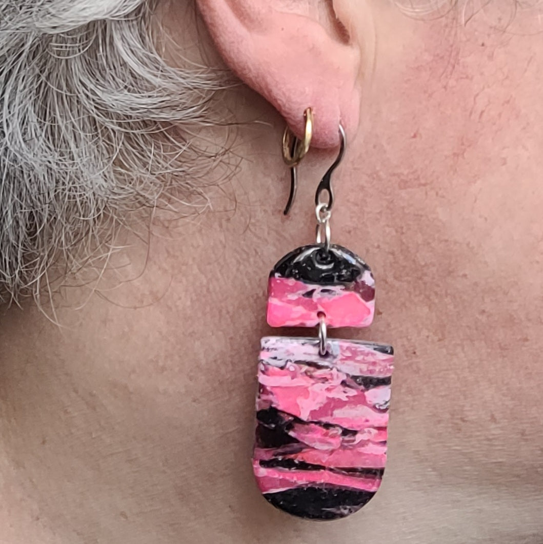 Boucles d’oreilles pendantes Nyméria en pâte polymère et résine, marbrées rose et noir, photographiées portées.