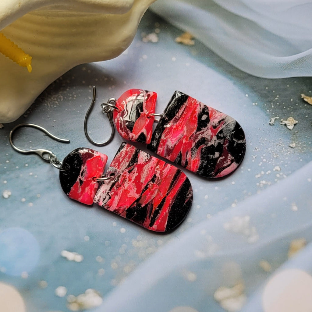  Boucles d’oreilles pendantes Nyméria en pâte polymère et résine, marbrées rose et noir, photographiées à plat.