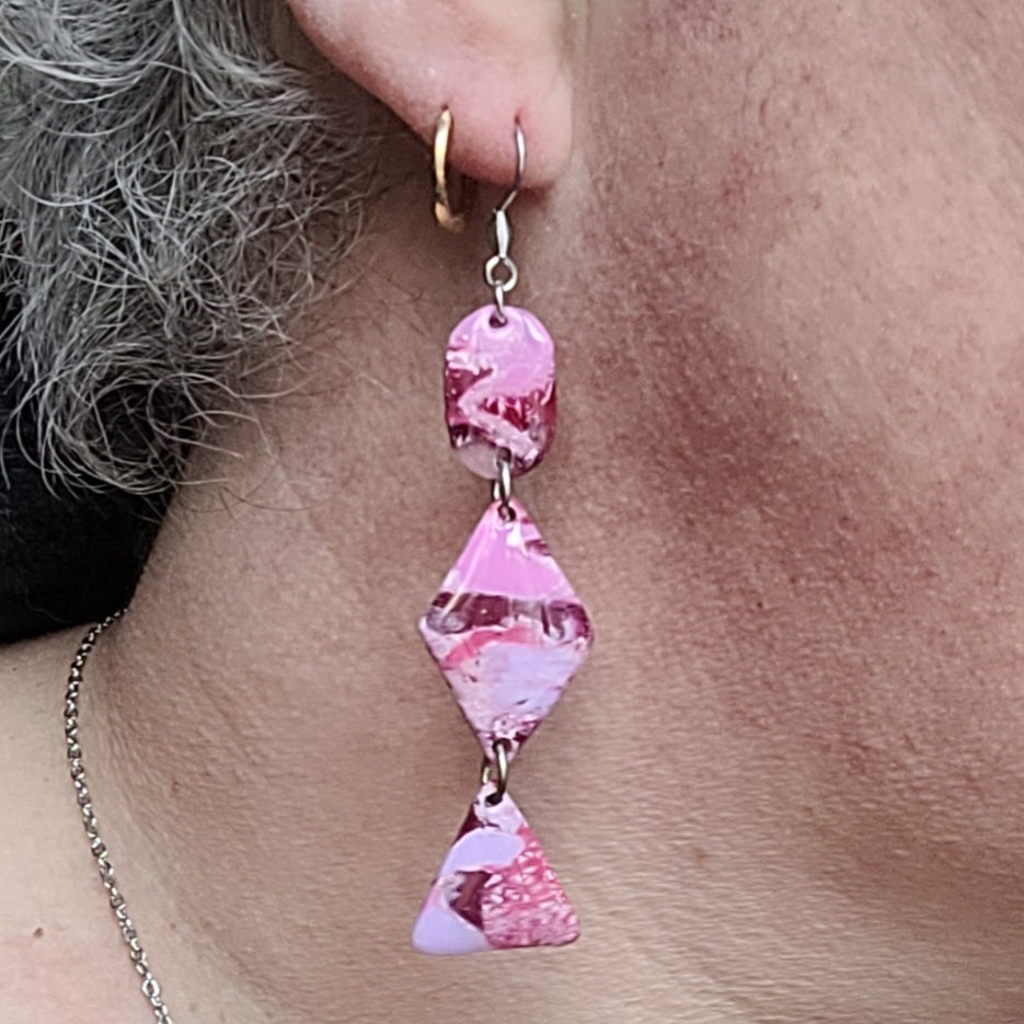 Boucle d’oreille Rétro-chic portée par Alysel Créations, avec trois formes géométriques articulées aux nuances roses, blanches et bordeaux