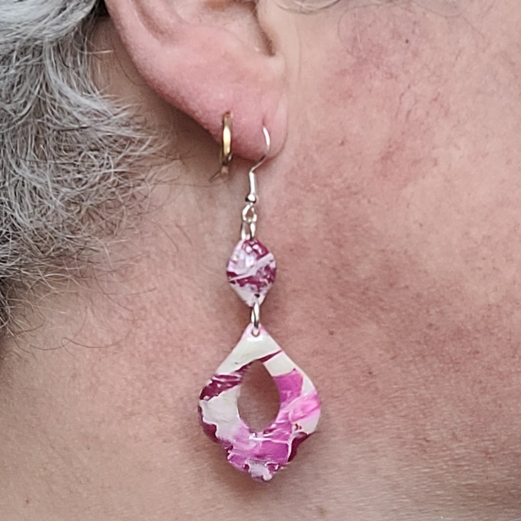 Boucle d’oreille Rétro-chic portée par Alysel Créations, montrant son pendentif ajouré aux contours ondulés et ses motifs roses, blancs et bordeaux.
