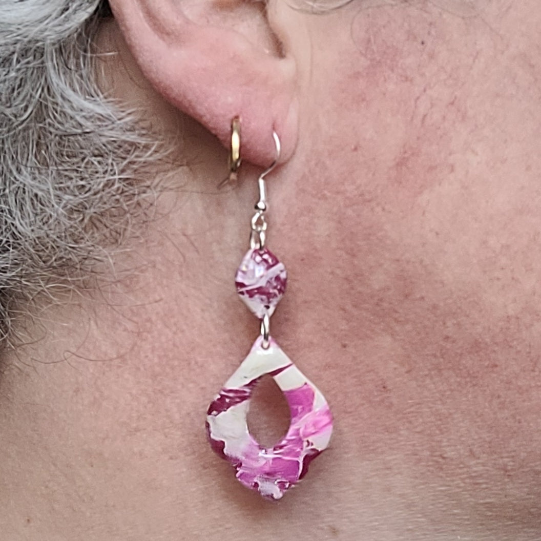 Boucle d’oreille Rétro-chic portée par Alysel Créations, montrant son pendentif ajouré aux contours ondulés et ses motifs roses, blancs et bordeaux.