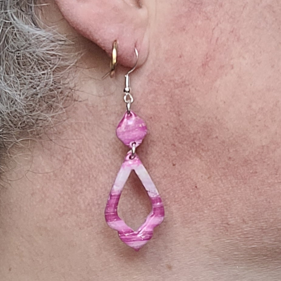 Boucle d’oreille Rétro-chic portée par Alysel Créations, avec un pendentif allongé ajouré aux nuances roses et blanches.